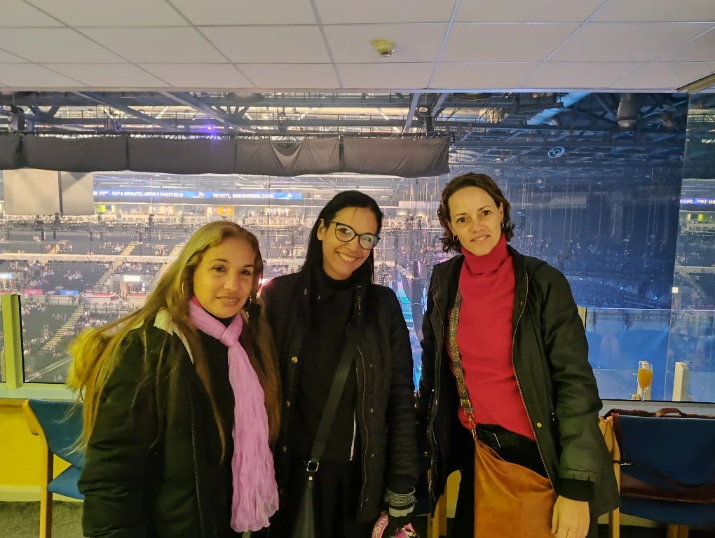 Three individuals standing in an indoor arena with seats and stage visible in the background.