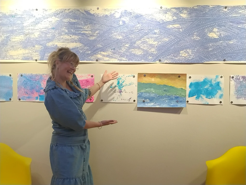 Person gesturing to artworks displayed on a wall.